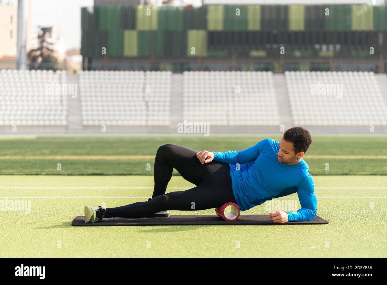 Stock photo of african american male athlete sitting on the track stretching his legs with foam roller. Stock Photo