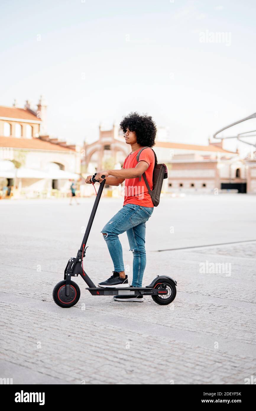 Stock photo of young black boy riding his electric scooter during sunny  day. He is wearing jeans and has cool afro hair Stock Photo - Alamy