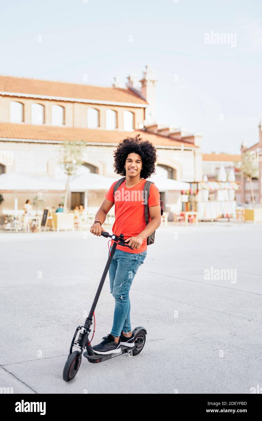 Stock photo of happy black boy riding his electric scooter during sunny  day. He is wearing jeans and has cool afro hair Stock Photo - Alamy
