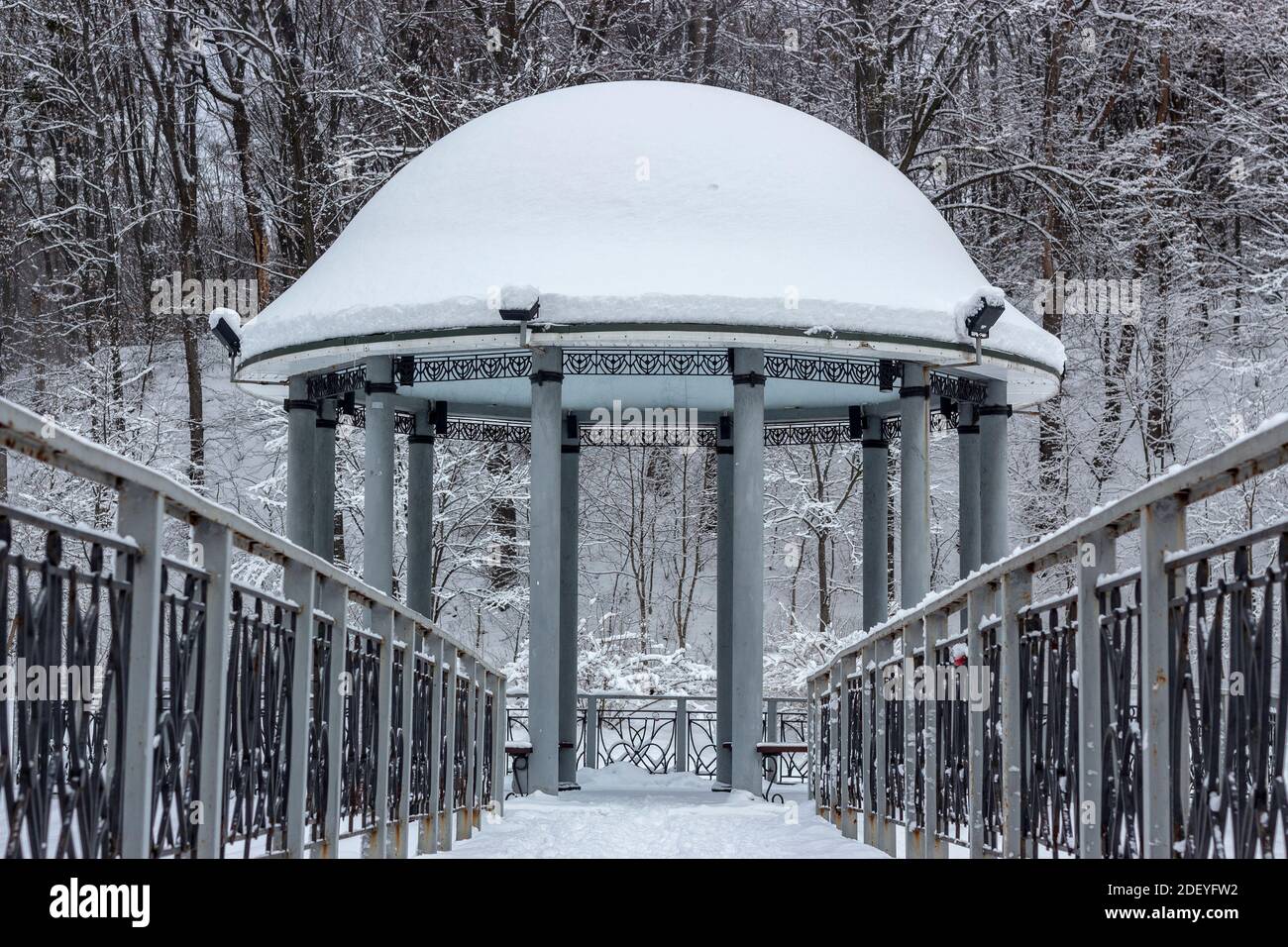 Snow-covered gazebo with a metal bridge in the middle of a lake in the ...