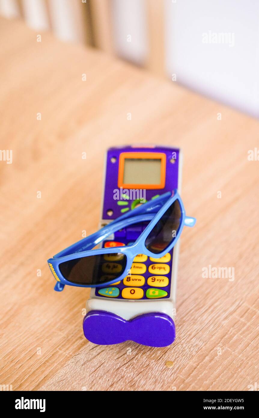 POZNAN, POLAND - May 22, 2016: Fisher Price toy telephone and blue sunglasses on a wooden table Stock Photo