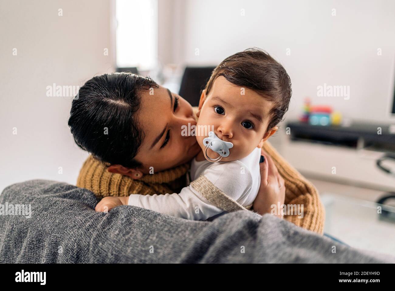 Stock photo of young mother kissing her little baby in the sofa. Stock Photo