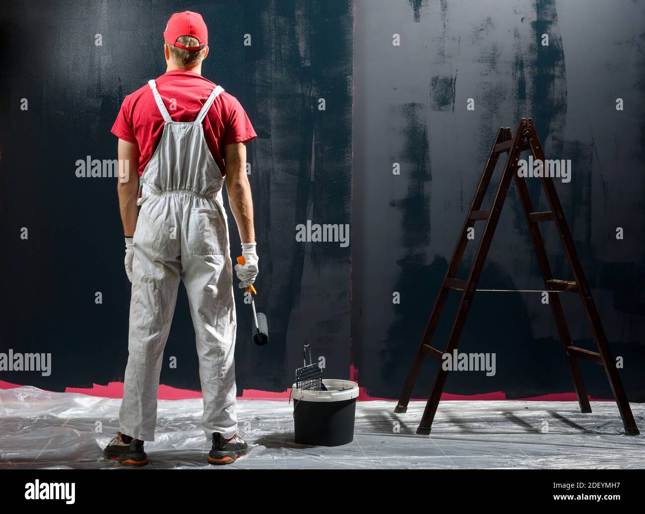Man painting a wall. Painter in red overall painting wall in black color Stock Photo Alamy