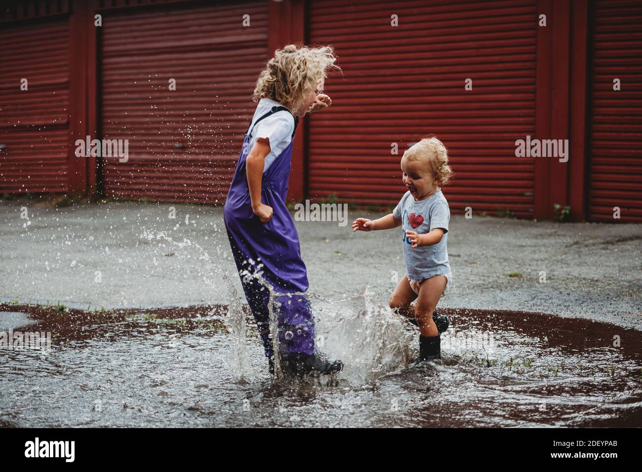 Girl and boy splashing in the water after the rain and laughing Stock Photo