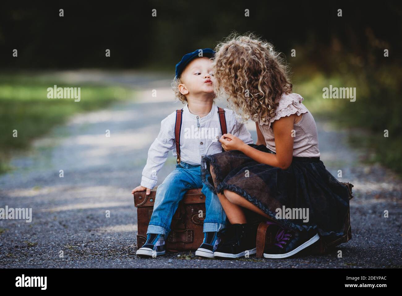 Adorable children siting on a vintage suitcase throwing a kiss Stock Photo