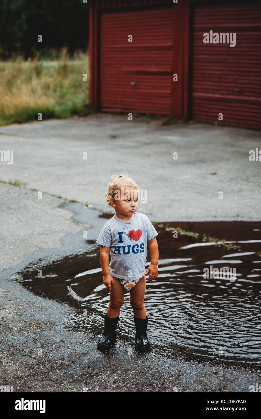 Adorable young boy pouting wearing rubber boots next to a puddle Stock Photo