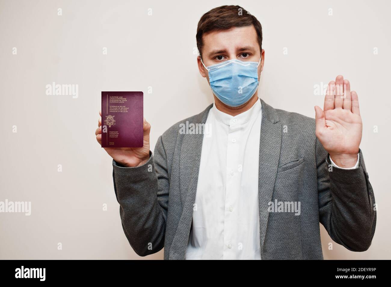 European man in formal wear and face mask, show Belgium passport with