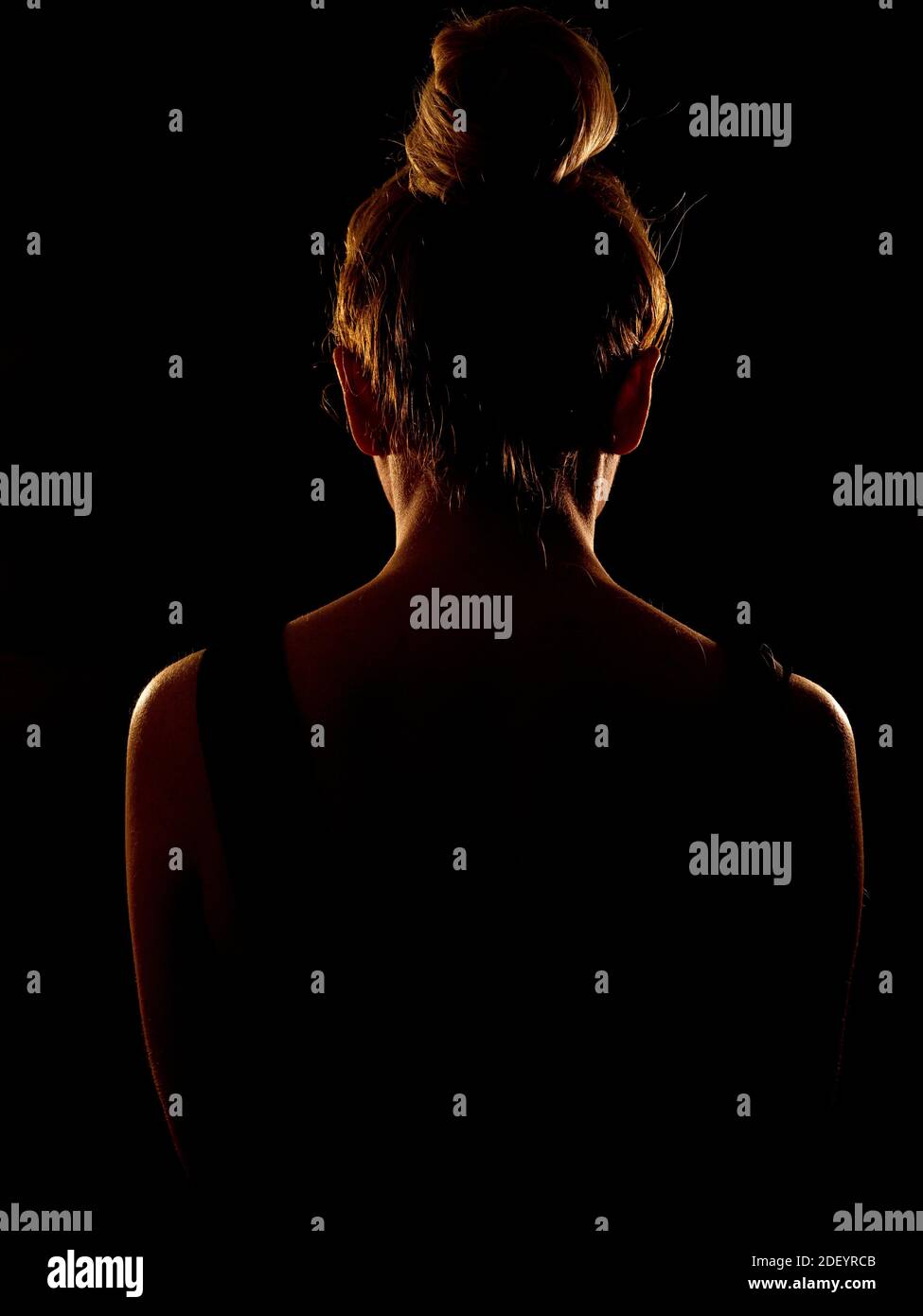 rear view of a woman with hair in a bun, in rim light Stock Photo