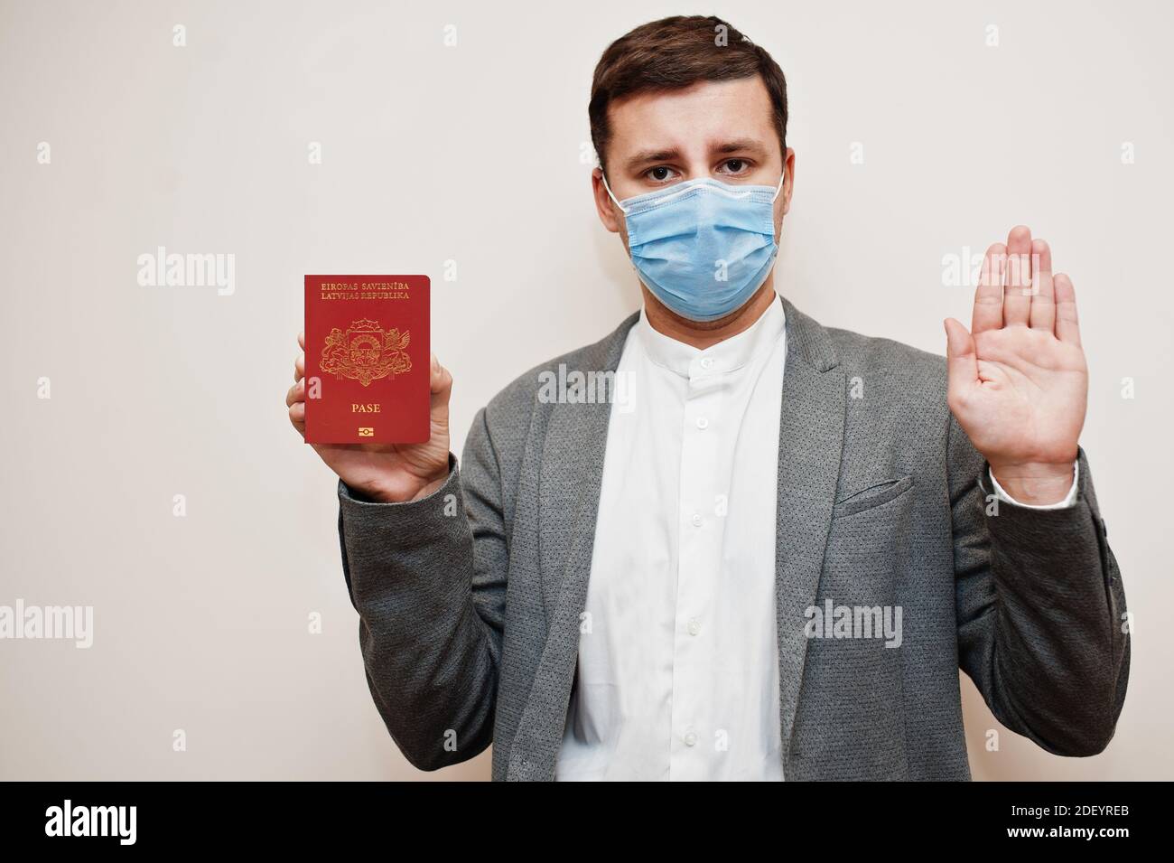 European man in formal wear and face mask, show Latvia passport with