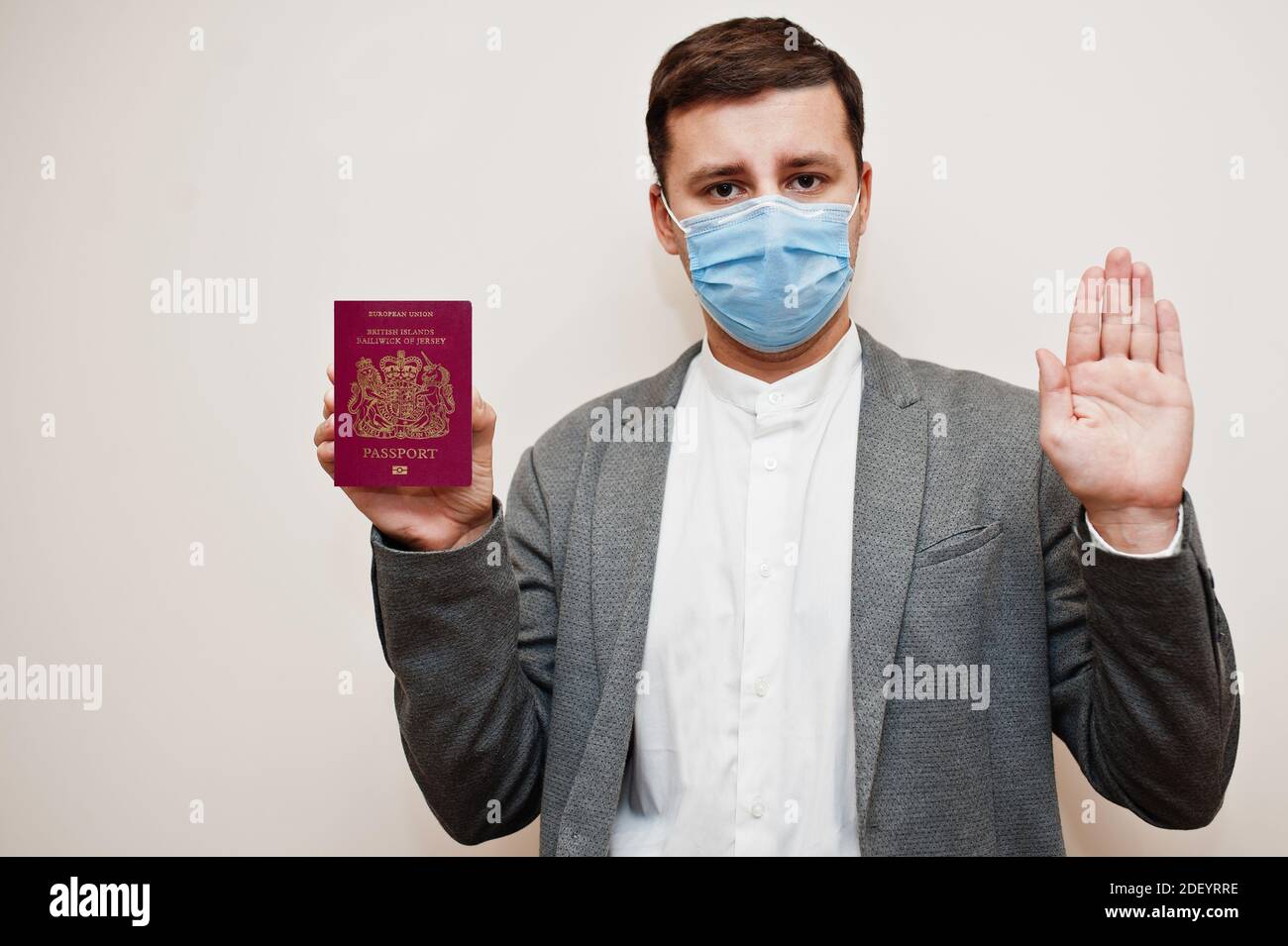 European man in formal wear and face mask, show Bailiwick of Jersey passport with stop sign hand. Coronavirus lockdown in Europe country concept. Stock Photo