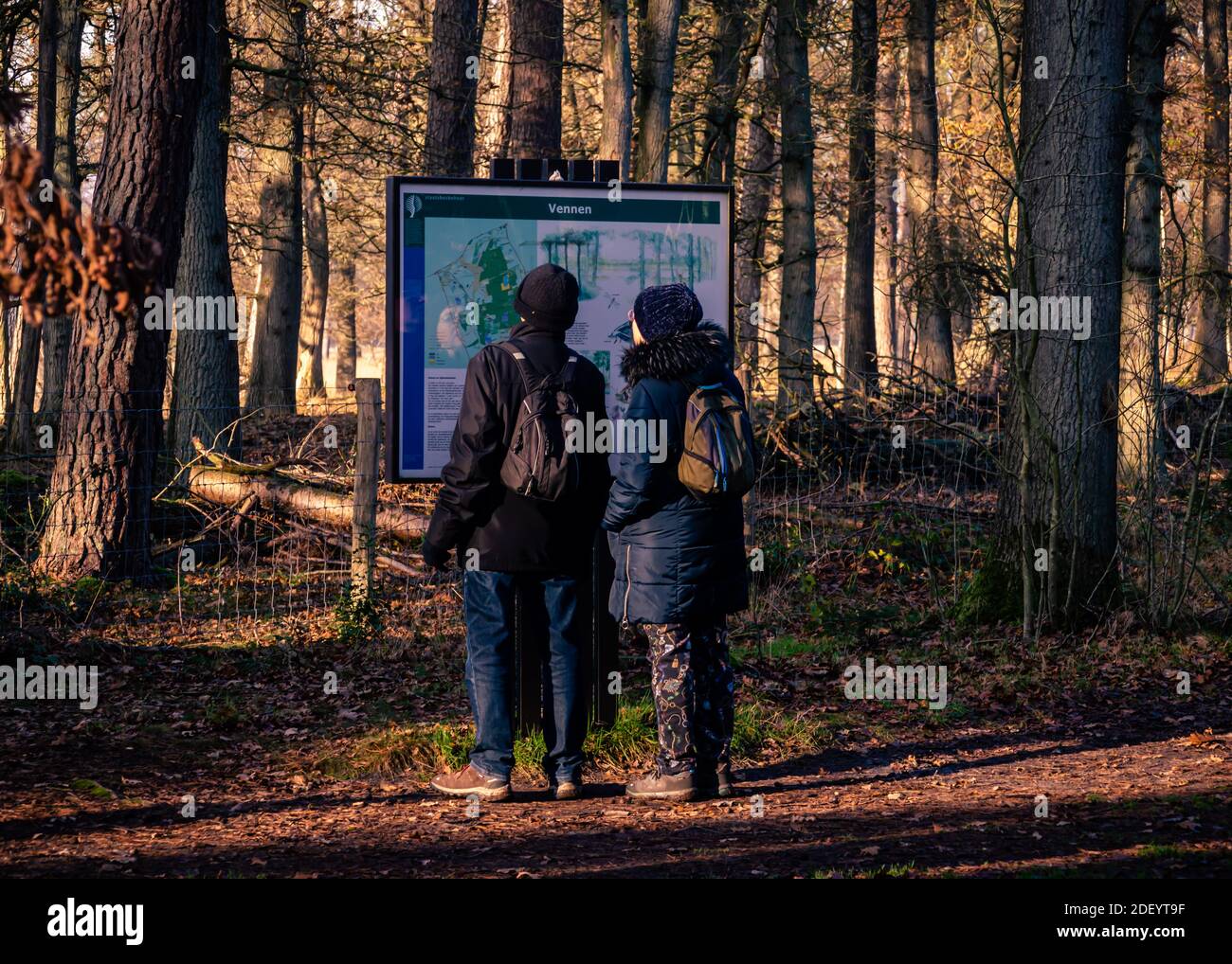 BORGER, THE NETHERLANDS NOVEMBER 25, 2020: Two people with small backpacks, wearing thick winter coats and warm woolen hats looking at the information Stock Photo