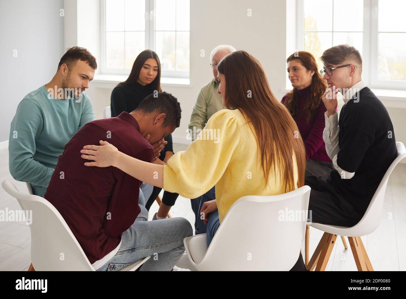 Diverse people supporting and comforting crying young man in group therapy session Stock Photo