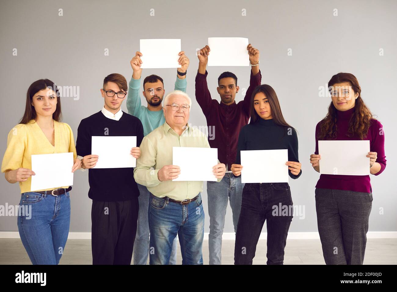 Group of different people standing together, holding white sheets of paper and looking at camera Stock Photo