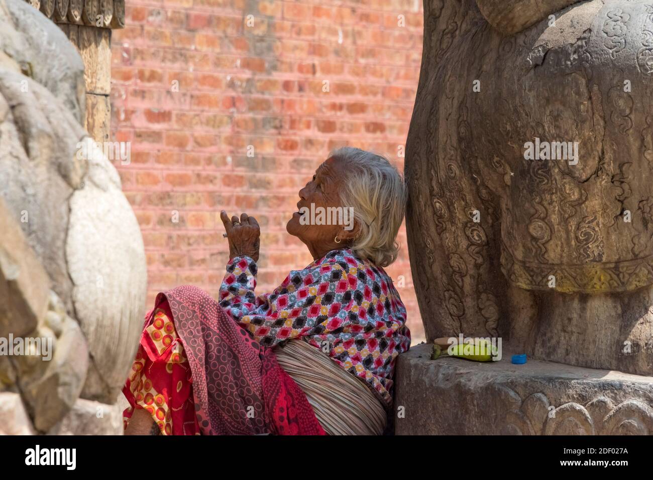 Woman smoking at the entrance to Nyatapola Temple (a five-storeyed pagoda style temple) in Taumadhi Square (part of Bhaktapur Durbar Square), UNESCO W Stock Photo