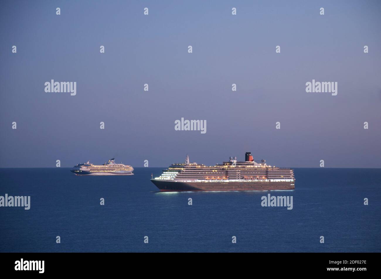 Cunard ocean liner Queen Victoria and cruise ship Marella Explorer anchored in Weymouth Bay at dusk. Mothballed during the Covid-19 pandemic. Dorset. Stock Photo