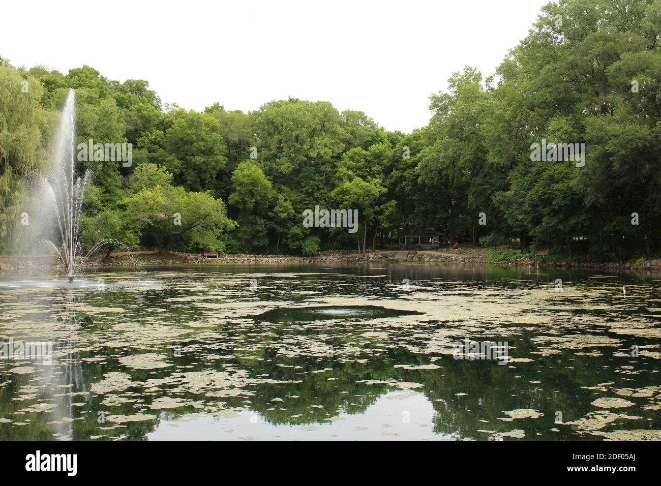 A water fountain in a lake surrounded by walking paths, trees, benches and a gazebo in Rotary Botanic Gardens, Janesville, Wisconsin, USA Stock Photo