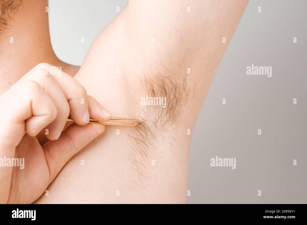 Man remove hair using tweezers from armpit. Unshaved armpits or underarm. Depilation and hair remove procedure, Body shaming concept Stock Photo
