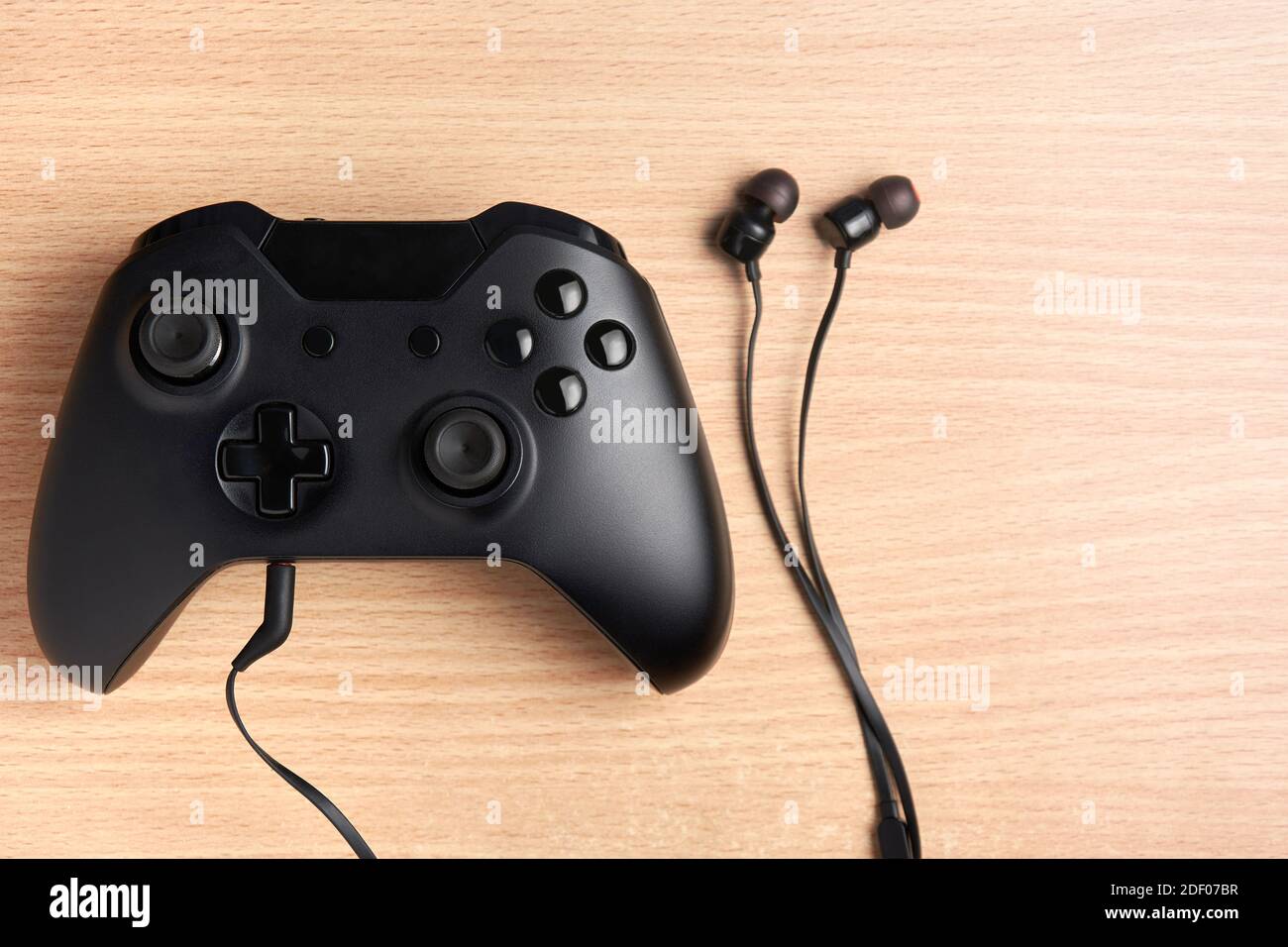 Black video game controller with earphones connected to it on wooden desktop. Stock Photo