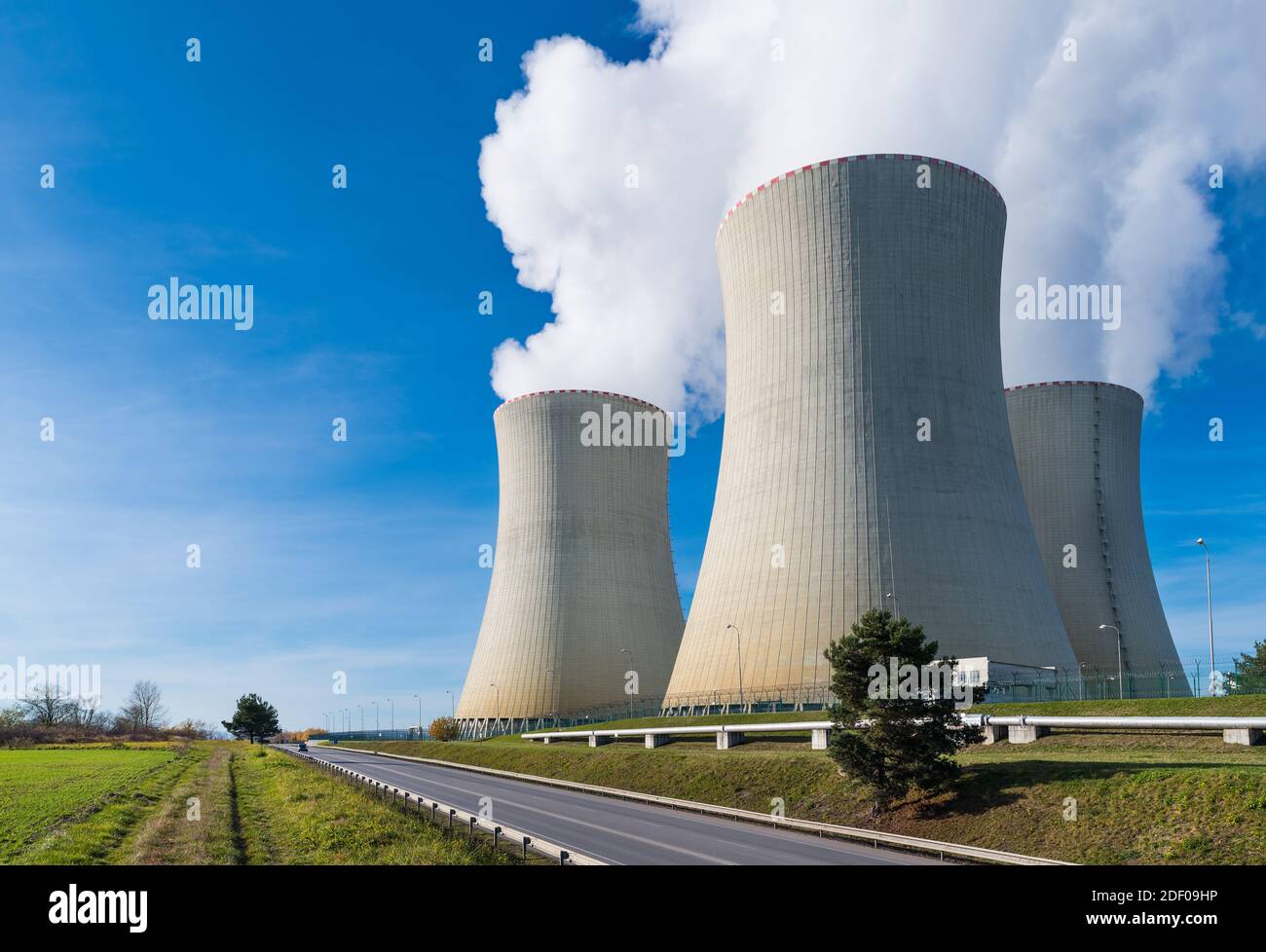 Nuclear power plant cooling towers with water vapor plumes on blue sky background. Modern generating station in landscape, road and steam piping. Eco. Stock Photo