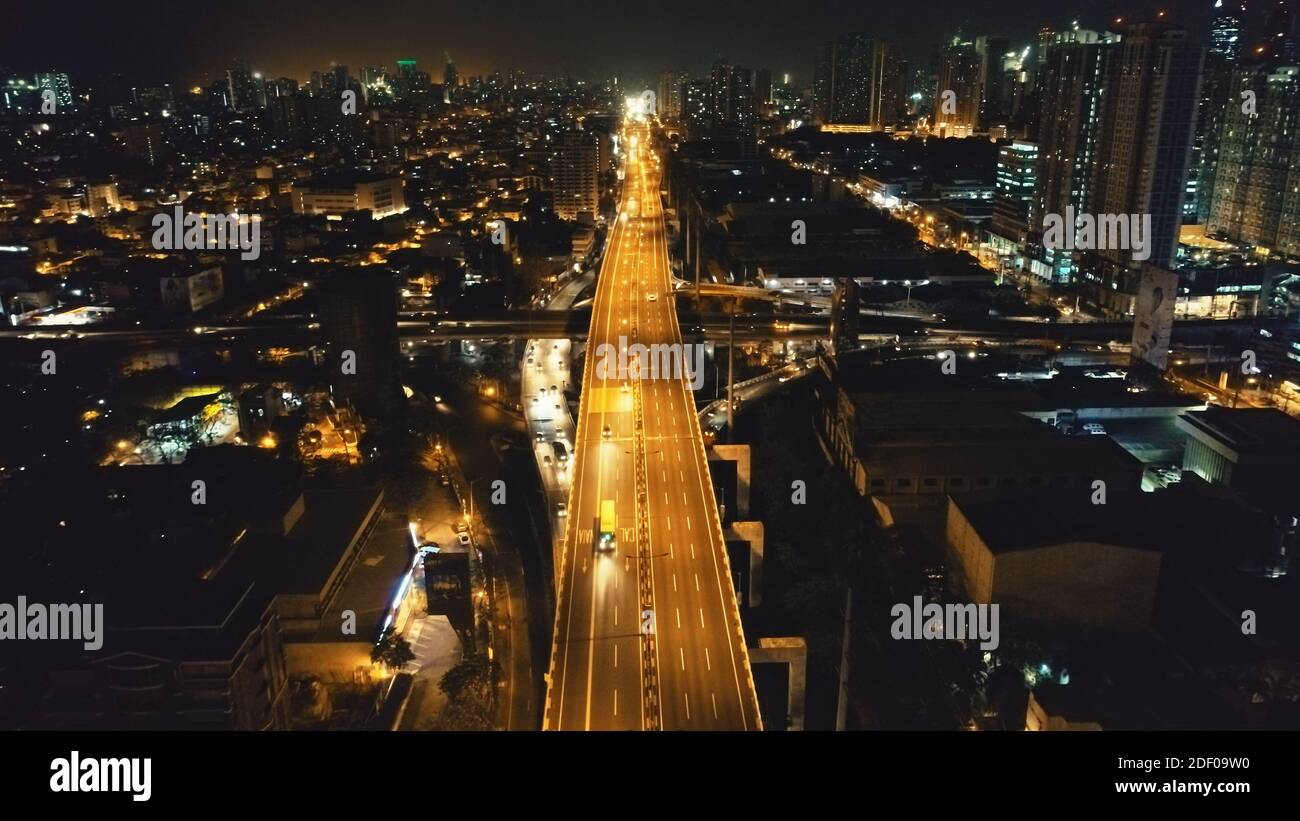 Night illuminated cityscape with traffic highway at business centre aerial. Epic twilight city in neon light at lit by lanterns road with cars, trucks ride. Philippines capital town of Manila streets Stock Photo