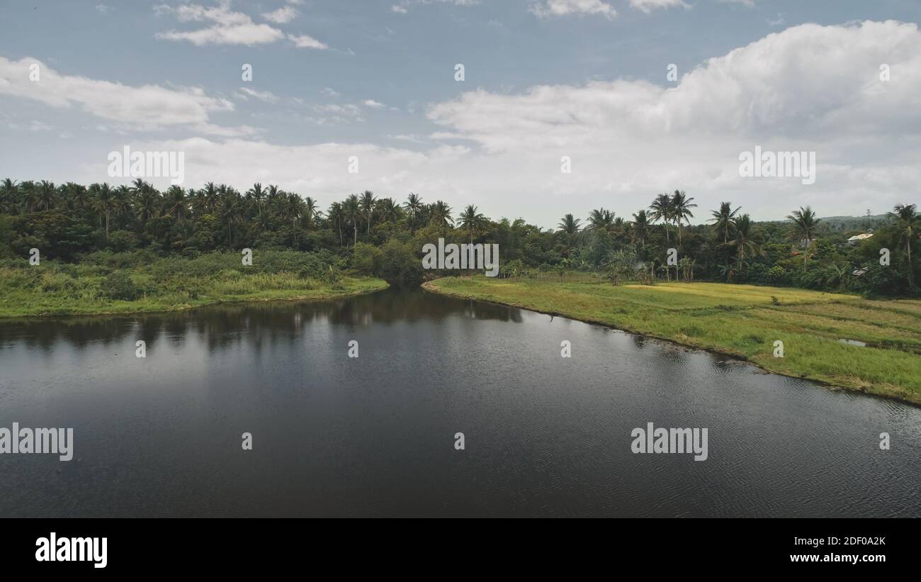 Mayon lake shore aerial. Nobody nature landscape with green grass coast. Cottages at greenery palm trees. Amazing seascape of Philippines mount at tropic forest. Cinematic soft light drone shot Stock Photo