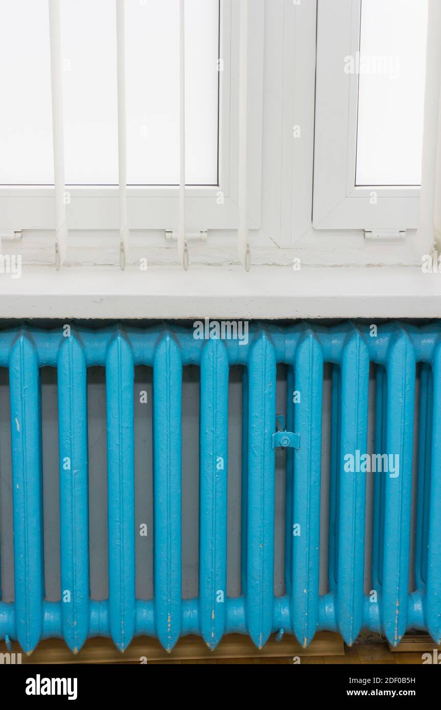 A vertical shot of a blue heating radiator behind the white windows ...