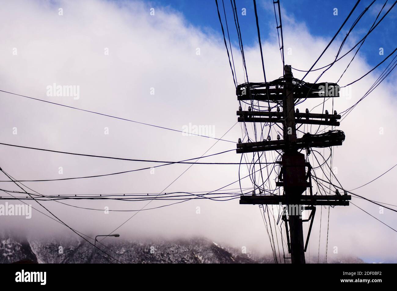 Complicated arrangement with messy electric wiring, white clouds in the background creating contrast Stock Photo
