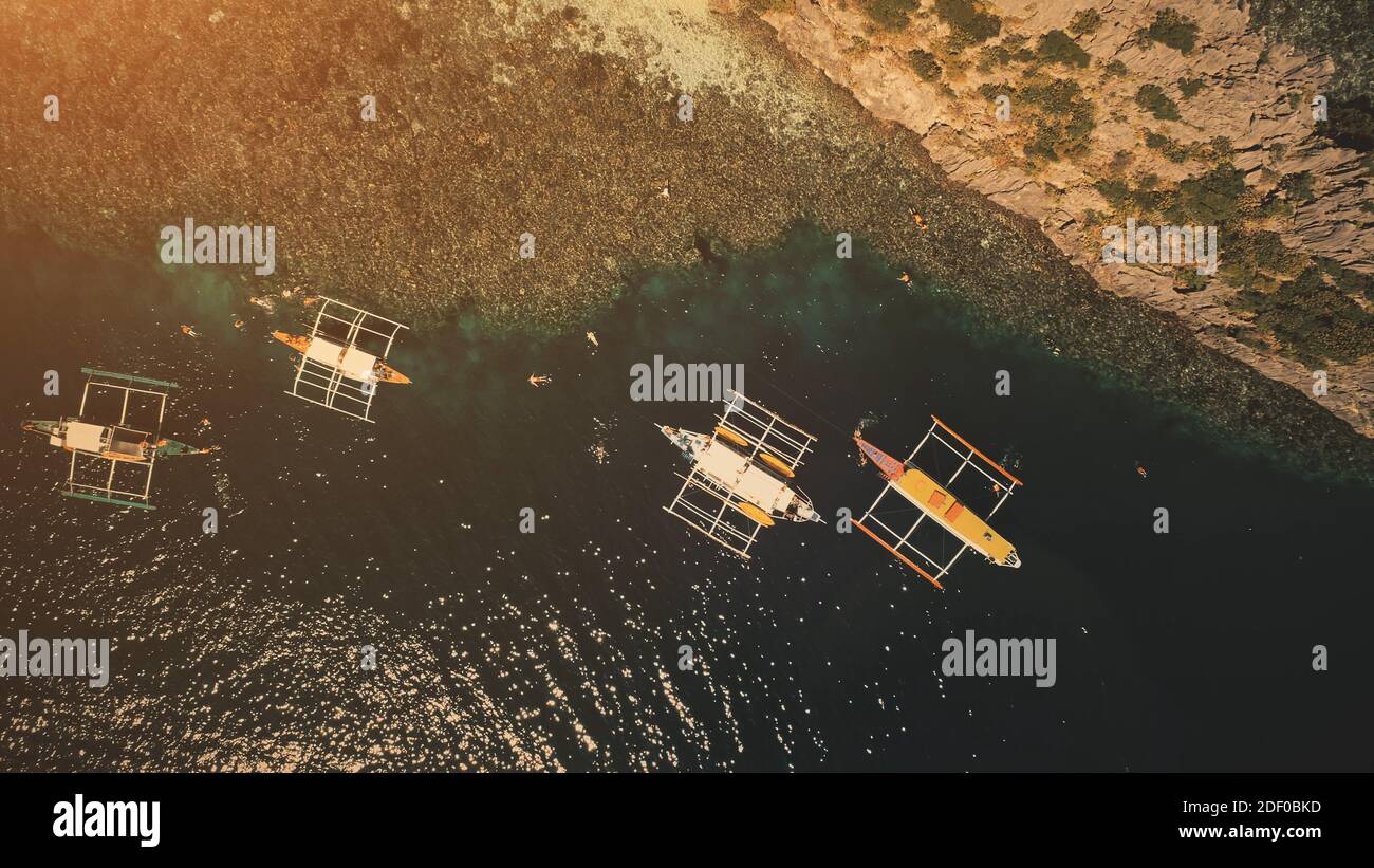 Sunset top down at ocean bay: passengers swim and dive at boats in aerial shot. Tourists leisure at summer cruise tour on traditional vessels. Philippines vacation at tropical island of Palawan Stock Photo