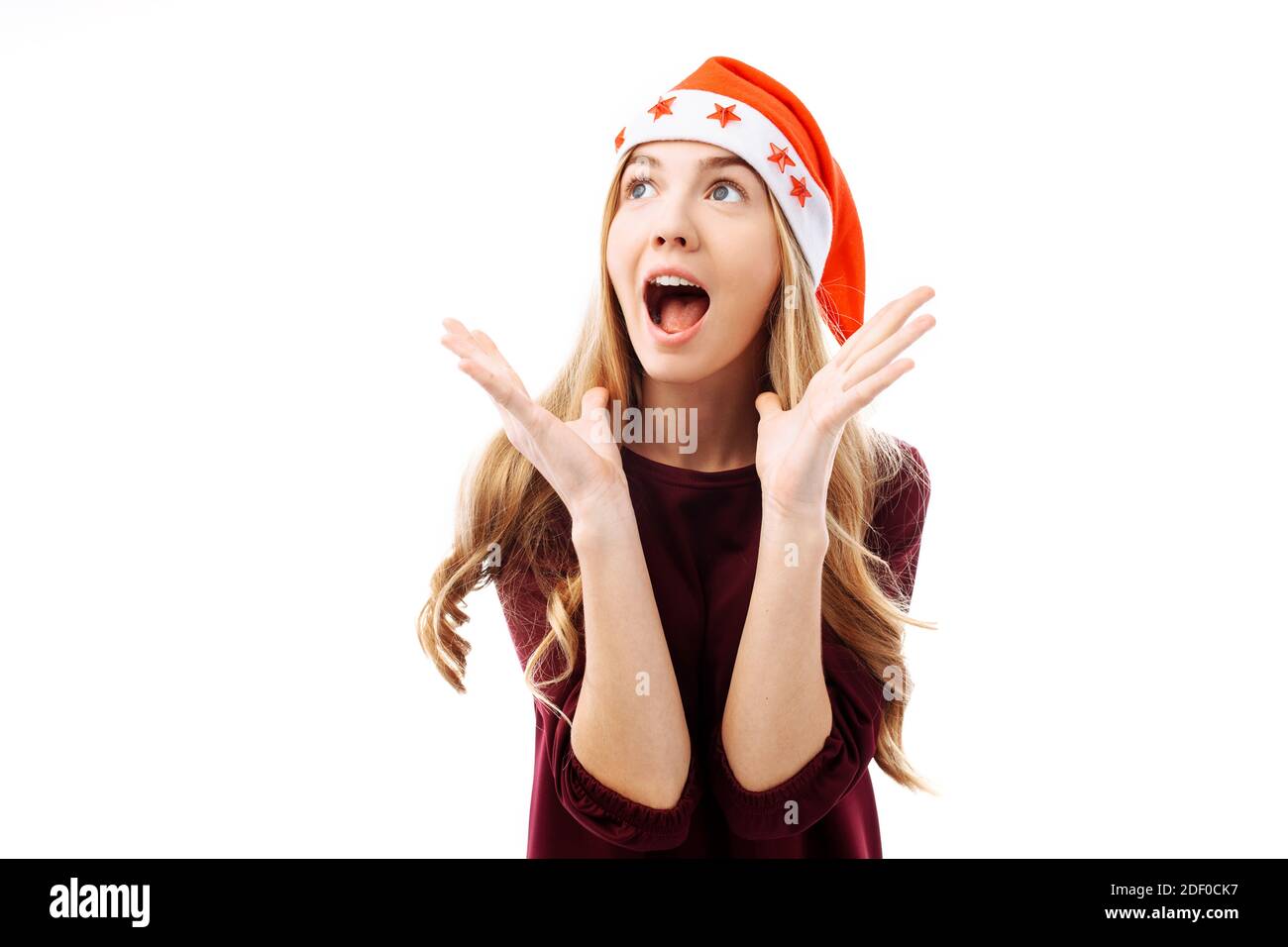 Excited beautiful girl in santa hat and dress, expressing happy emotions. Shocked and surprised girl screams. Christmas discounts Stock Photo