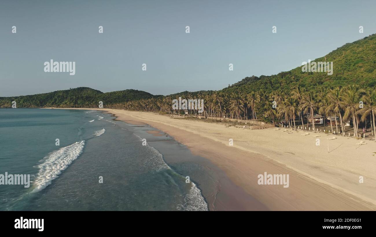 Waves washed sand ocean coast aerial. Tropical forest at paradise island. Nobody tropic nature seascape of El Nido Island, Philippines, Asia. Palm trees with lodges at sea bay Stock Photo