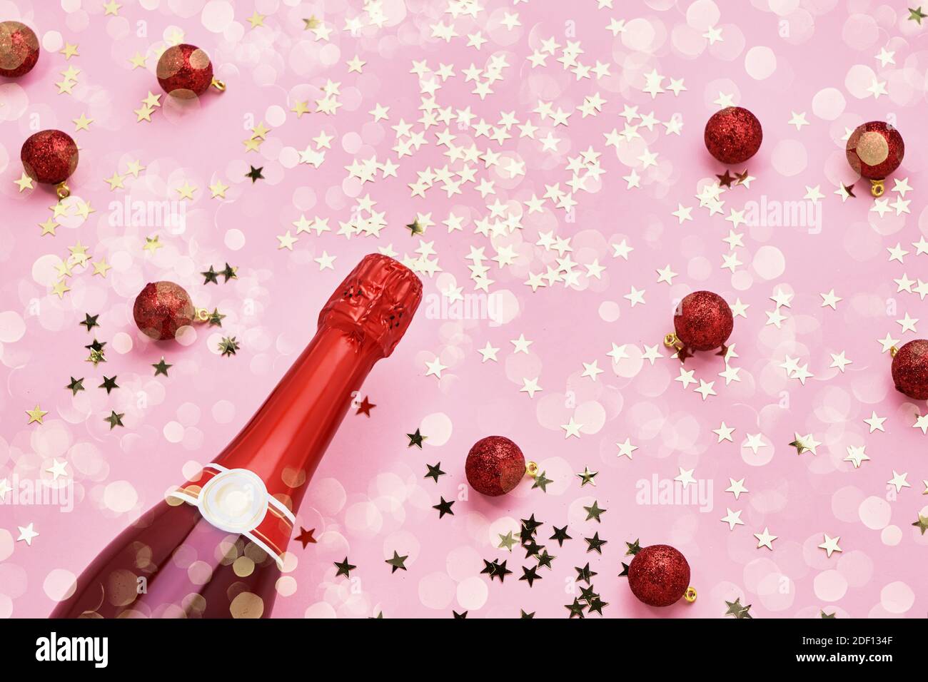Flat lay of Christmas Celebration. Champagne bottle with red Christmas decoration on pink background. Top view, copy space. Stock Photo