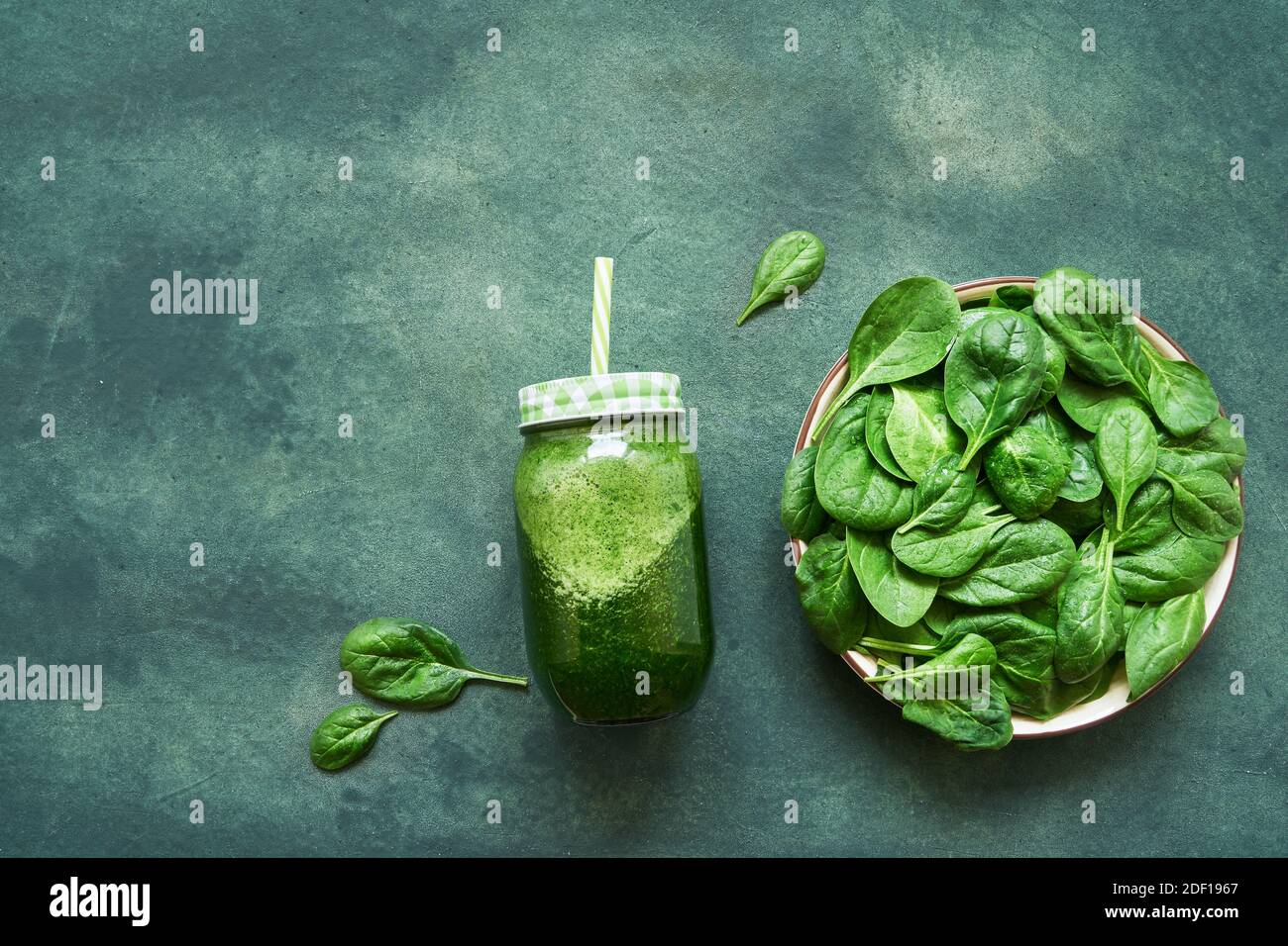 Green smoothie from spinach and kale in glass jar and plate with fresh spinach on green background. Healthy food flat lay. Copy space Stock Photo