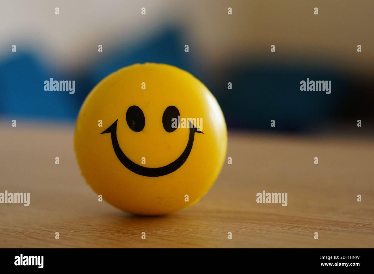A shallow focus shot of a yellow smiley stress ball on a table with a blurred background Stock Photo