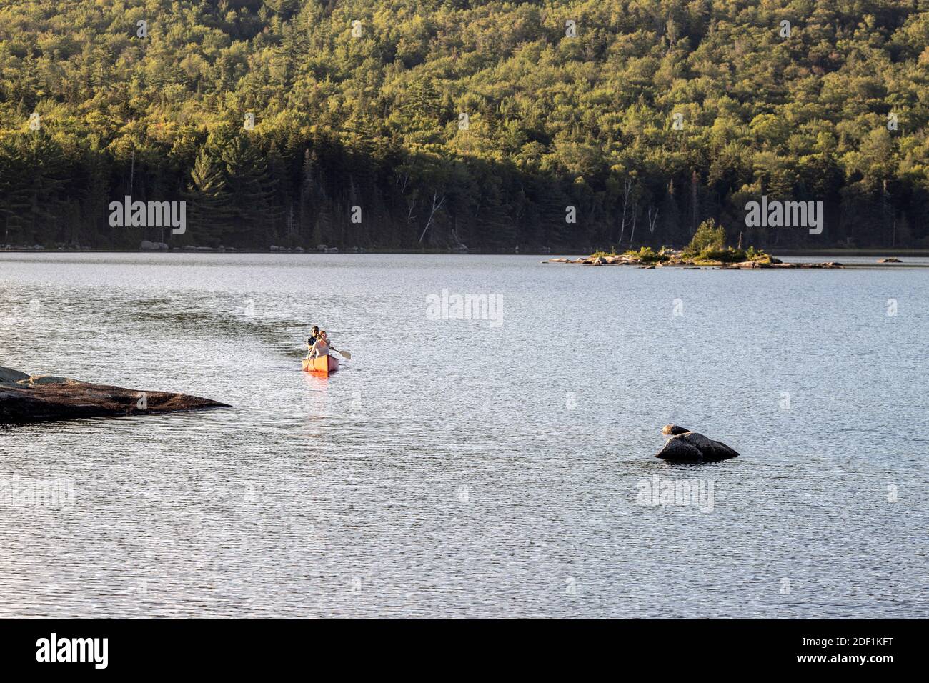 Two people paddle canoe across rocky Bald Mountain Pond in Maine Stock