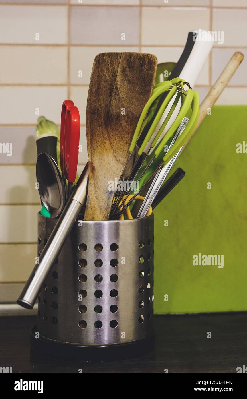 A mix of kitchen cooking utensils in a metal holder on a kitchen