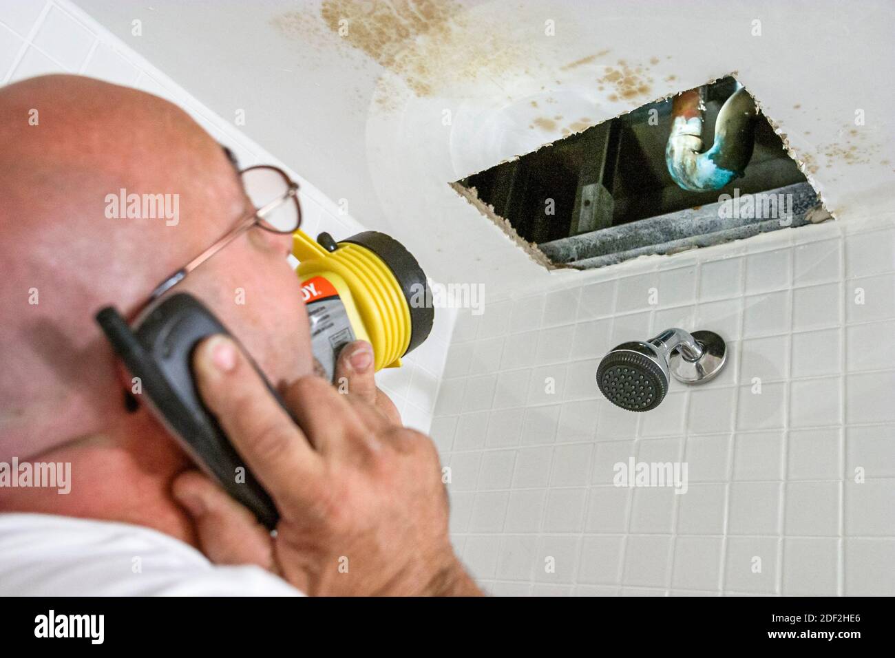 Miami Beach Florida,Hispanic man plumber,repairing repairs broken leaking pipe,calls calling owner using smartphone flashlight, Stock Photo