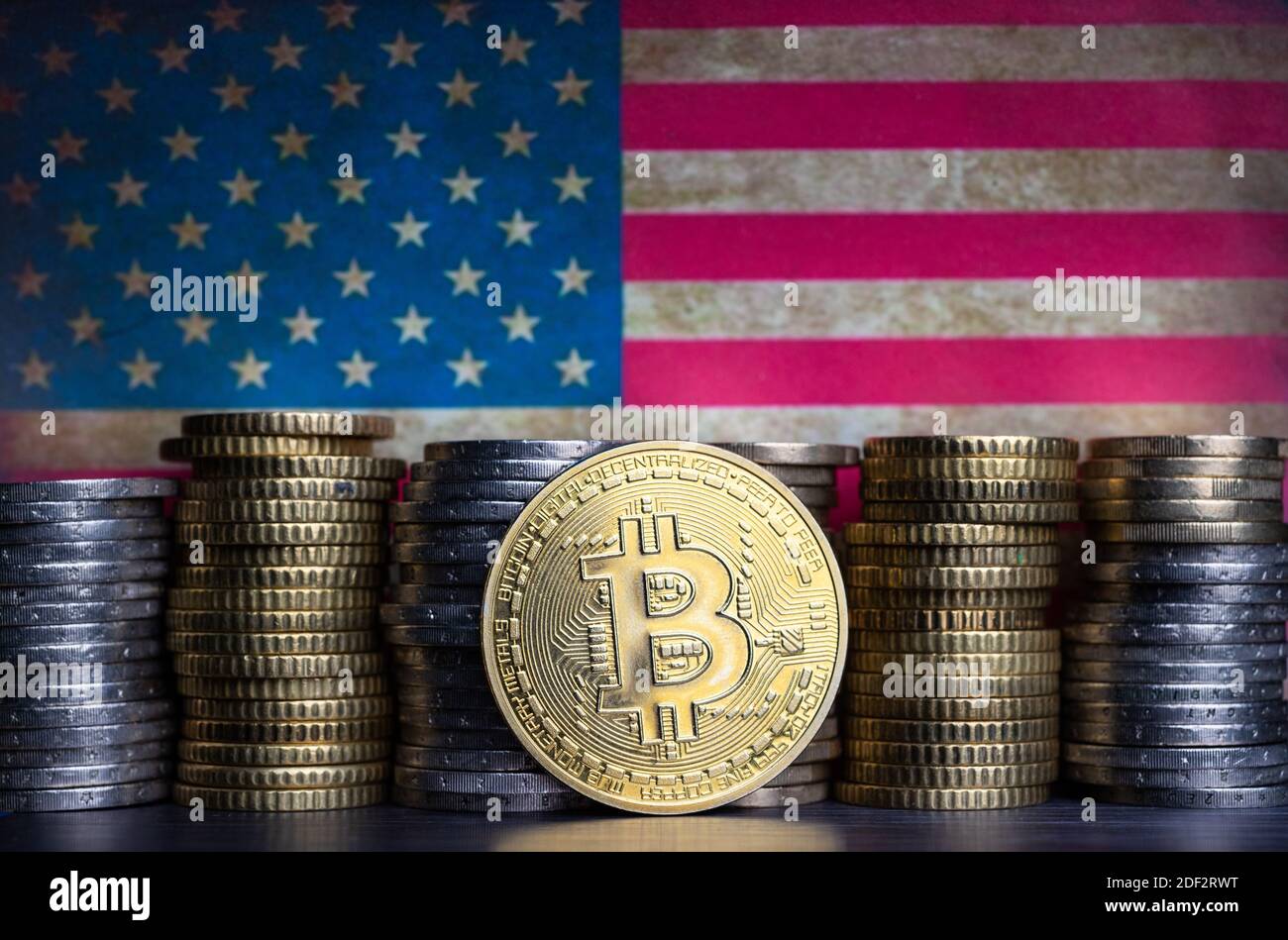 Bitcoin token infront of currency coins and grungy flag of the united states. Stock Photo
