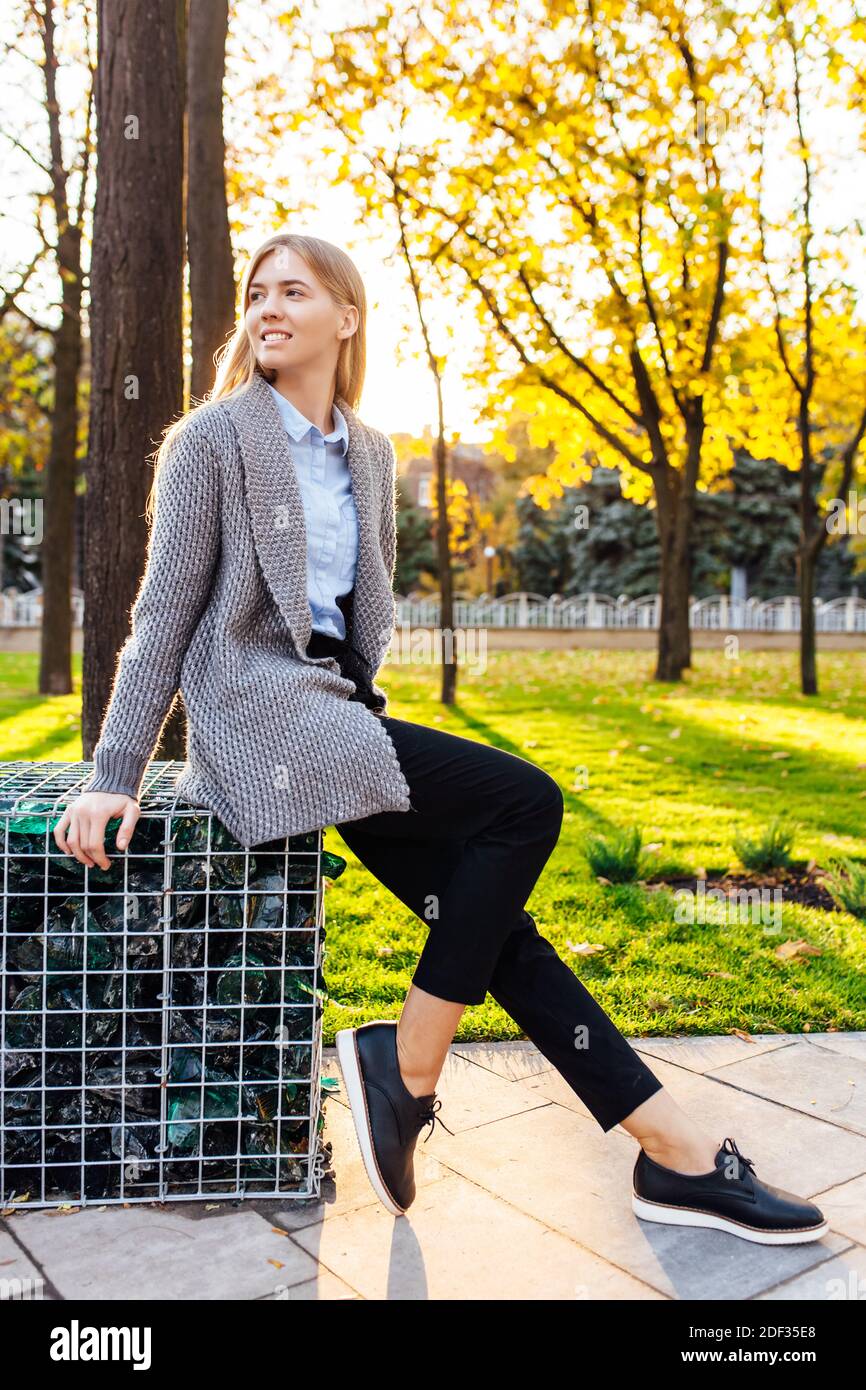young woman sitting on a park bench and laughs. nice girl in a good mood, on an autumn day, enjoying the good weather. Stock Photo
