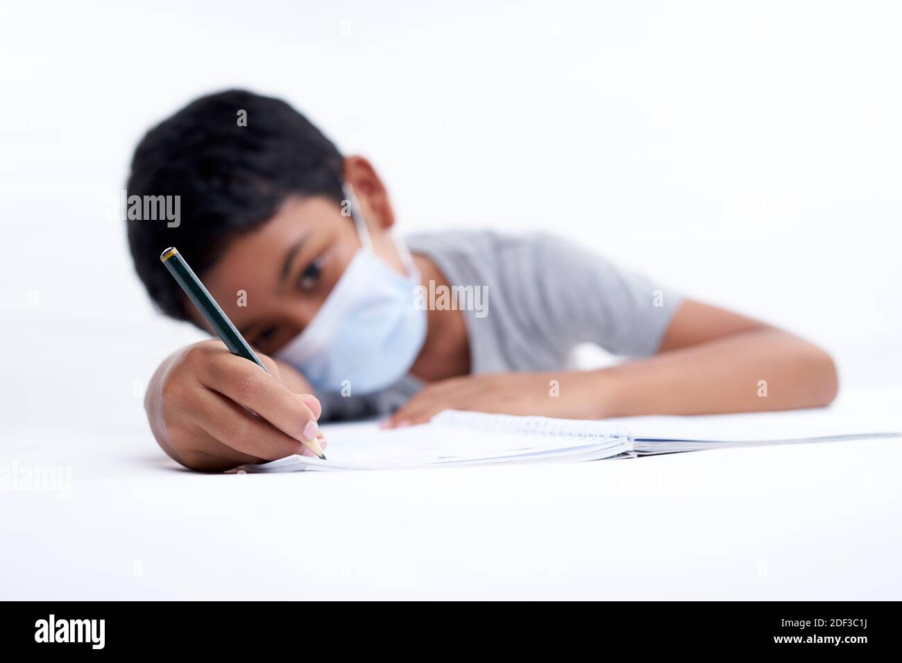 Schoolboy with protective face mask tired doing study and homework at home. new normal education concept Stock Photo