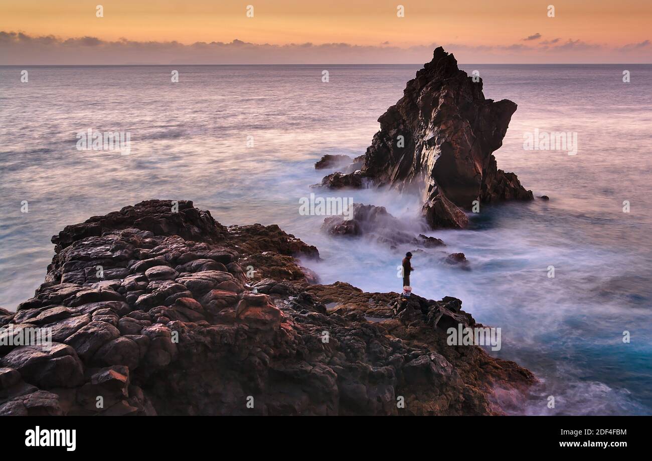 Silhouette of fisherman fishing on the Atlantic Ocean rugged coast during colorful sunrise, waves, rough sea, Funchal, Madeira, Portugal Stock Photo