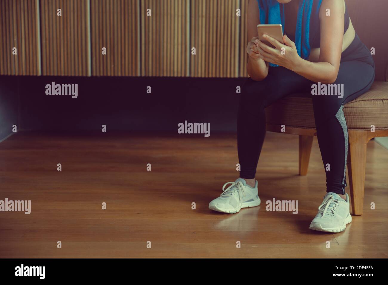 Sportswoman sitting and using smartphone in locker room at gym. Stock Photo