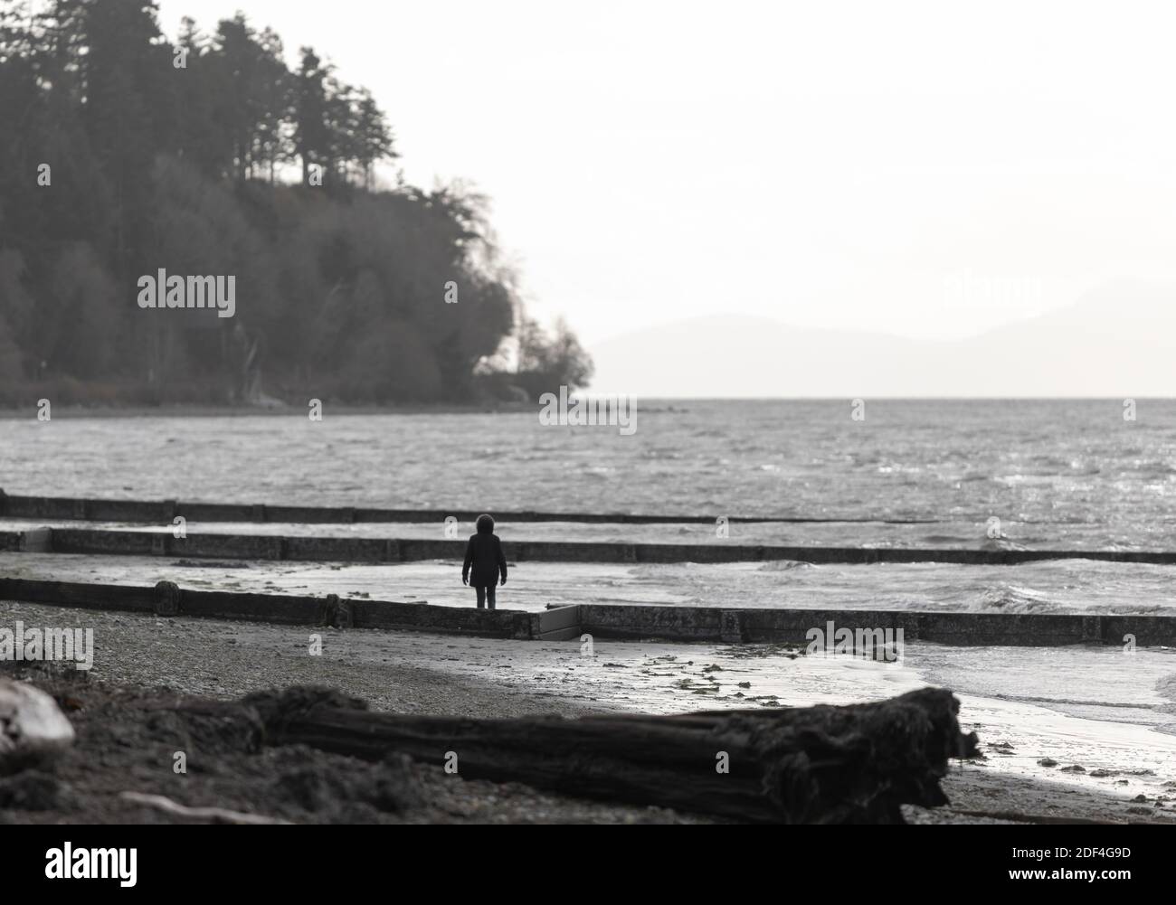 Landscape of a shoreline of the beach and a silhouette of a walking woman in a cloudy cold day. Selective focus, travel photo. Stock Photo