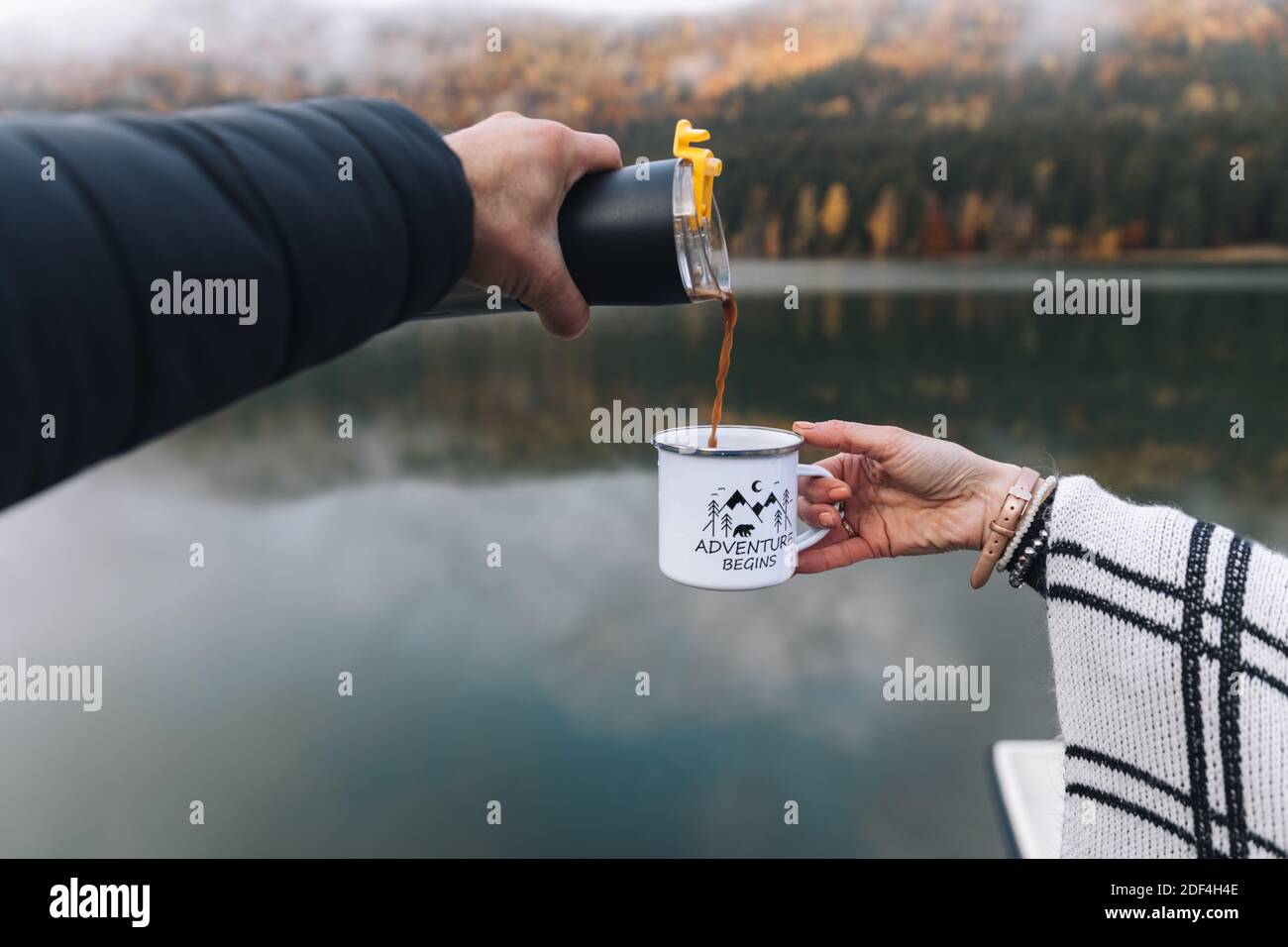 Traveler man pouring a hot drink from thermos to mug. Young woman drinking hot drink at cup. Autumn season.Outdoor Couple,Travel concept. Stock Photo