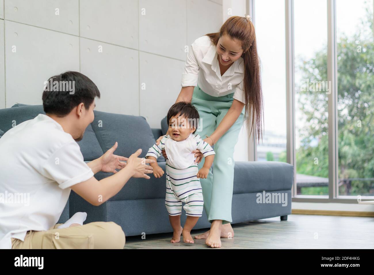 Asian son baby taking first steps walk forward to his father. Happy little baby learning to walk with mother help and teaching how to walk gentlyat ho Stock Photo