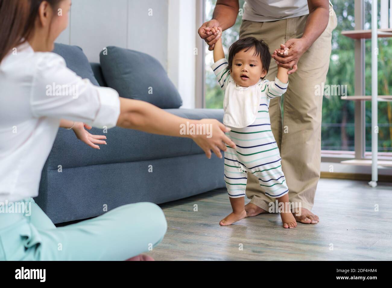 Asian son baby taking first steps walk forward to his mother. Happy little baby learning to walk with father help and teaching how to walk gentlyat ho Stock Photo