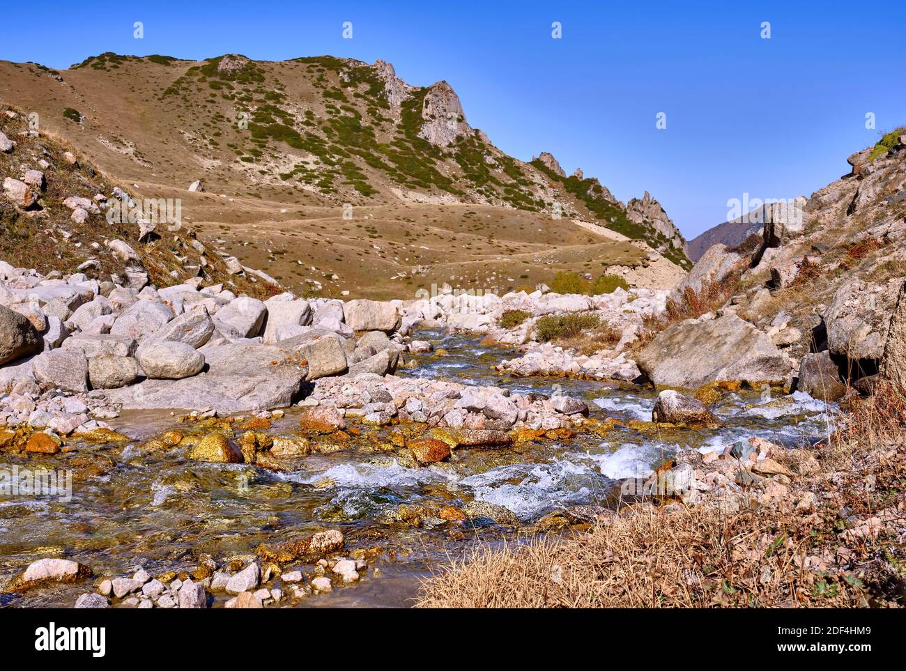 Alpine valley with a river and juniper-covered slopes on the background of  blue sky in autumn season Stock Photo