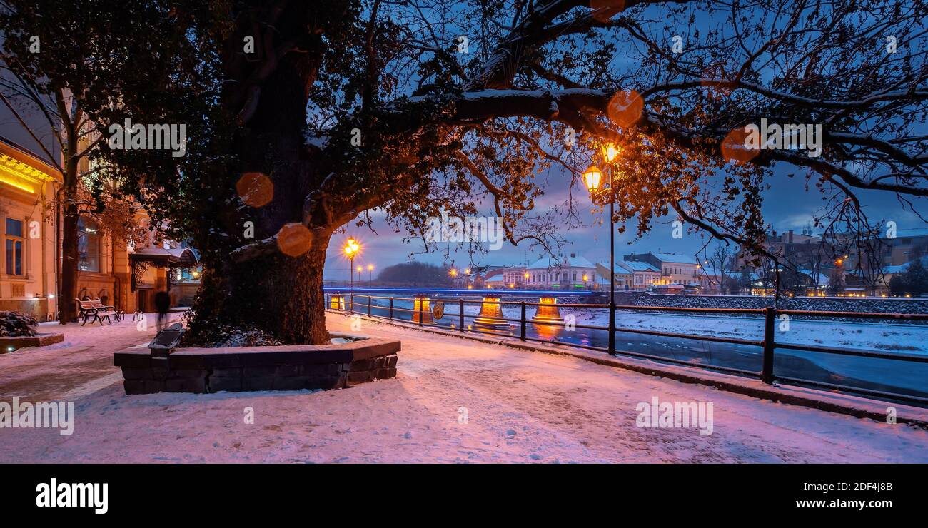 uzhhorod, ukraine - 26 DEC 2016: winter cityscape at dawn. beautiful scenery on the river uzh. city lights reflecting in the water. snow on the embank Stock Photo