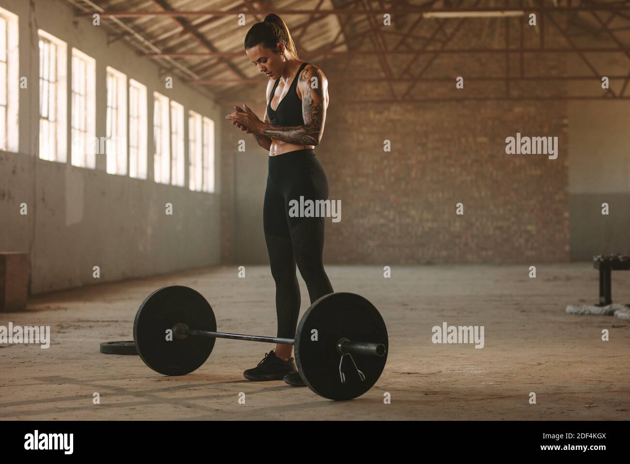 Strong female athlete standing with barbell on floor. Female athlete getting ready to lift barbell at old warehouse Stock Photo Alamy
