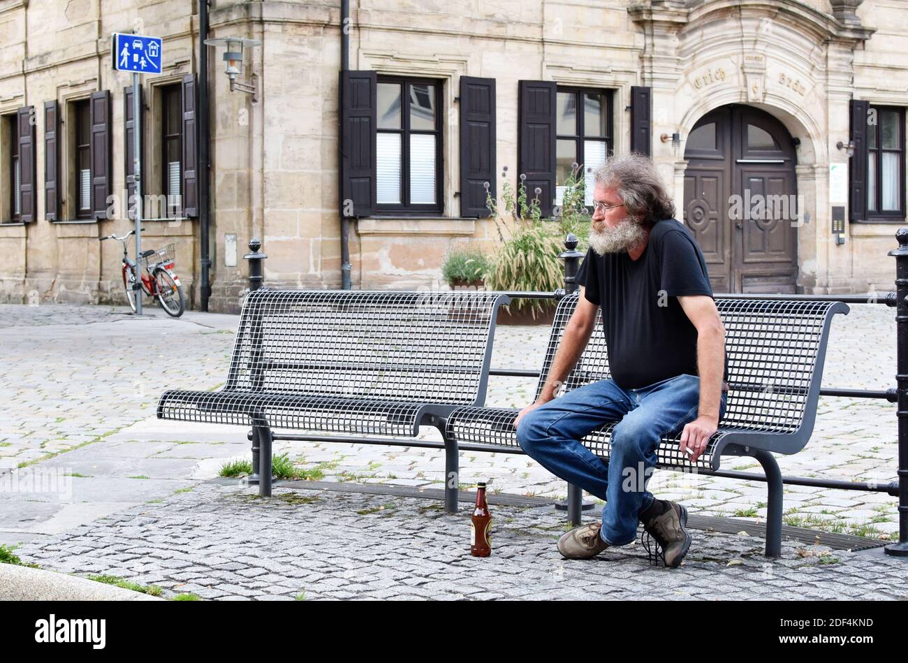 Man sitting (siting) on a bench, drinking and  smoking in the city center. Stock Photo