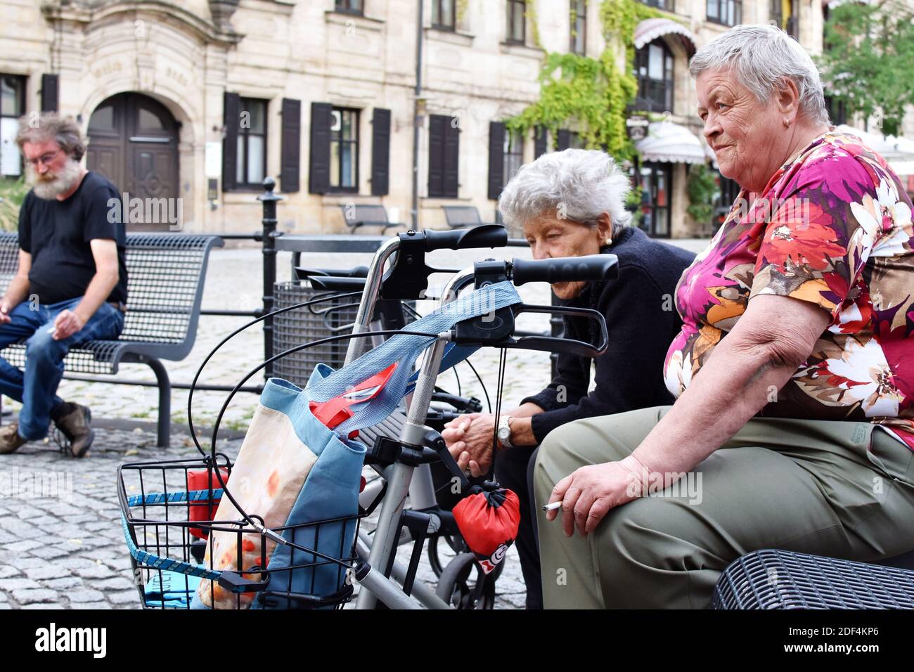 Two elderly women sitting on the bench and smoking in the city center Stock Photo